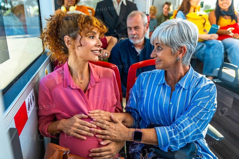 Pregnant woman receiving support and care from an elder woman, possibly her mother, as they travel together on a public transport bus, representing family connection and generational bonds