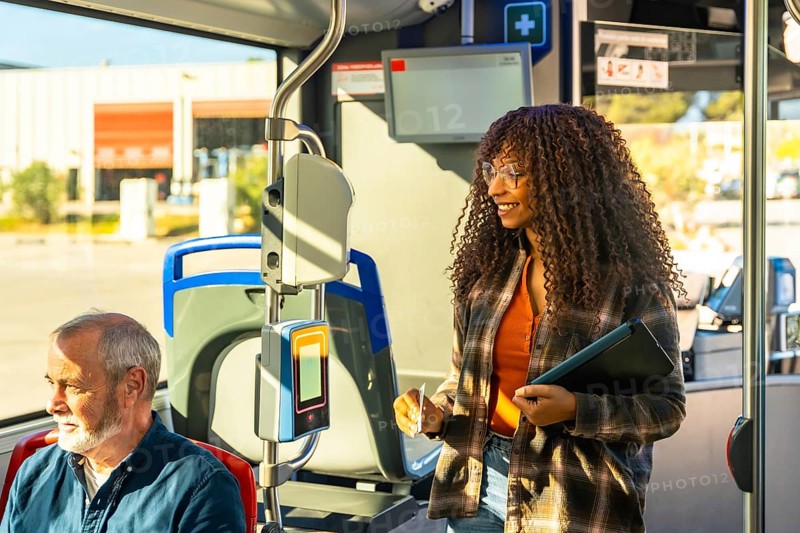 Young woman smiling while validating her transit card on a public bus, traveling in a city environment during her daily commute, with an older man sitting nearby
