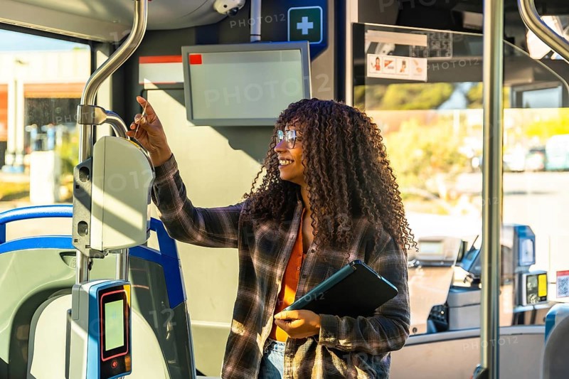 Young black woman holding a digital tablet and validating her public transport ticket on a modern bus, smiling as she is commuting and traveling by urban transit