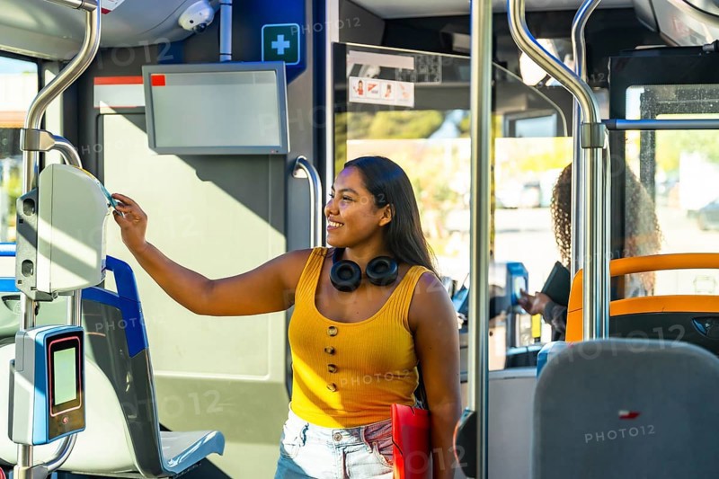 Young smiling woman using a payment validator for her ticket or travel card when boarding a city bus, promoting concepts of urban mobility and smart payment