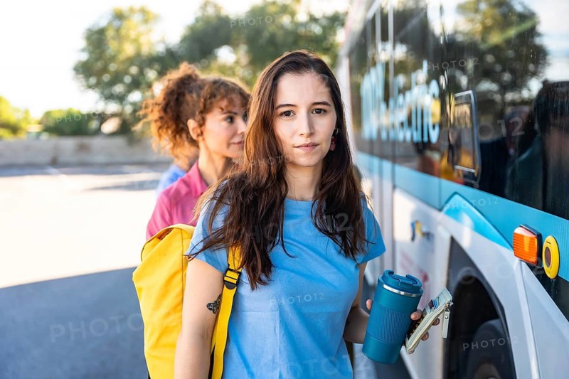Young female commuters are standing in line, holding a reusable cup and a wallet, waiting to board a public bus, reflecting sustainable and urban transportation concepts