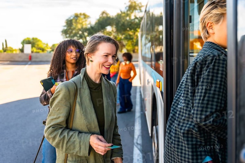 Happy woman smiling with bus ticket in hand, waiting in line to board a city bus for her daily commute using sustainable public transportation