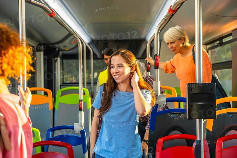 Diverse commuters stand and ride a bright city bus, holding handrails and chatting as they travel to work or around town, capturing everyday urban public transport life