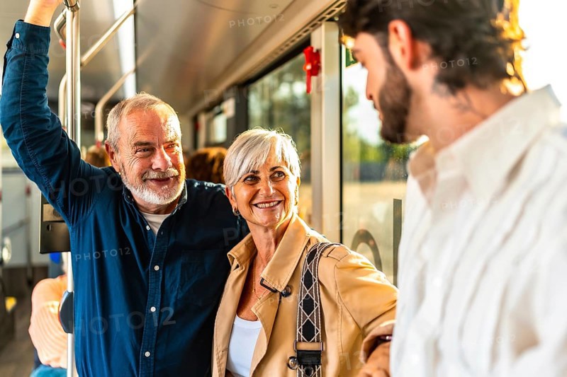 Happy senior couple chatting with a young man while riding a modern city bus, smiling and enjoying their urban journey, social connection and relaxed weekend commute