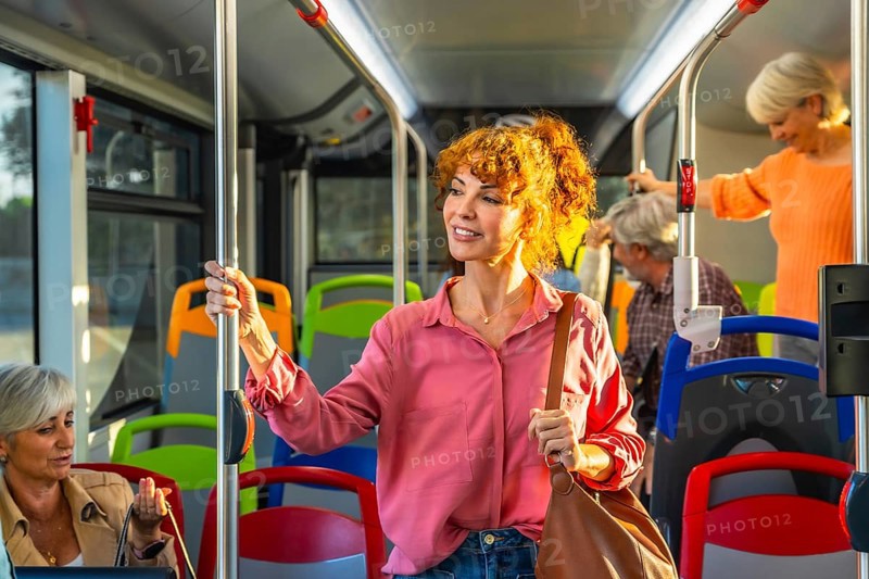 Woman standing on crowded city bus, holding a pole and smiling as she travels through the urban commute with fellow passengers during her daily journey
