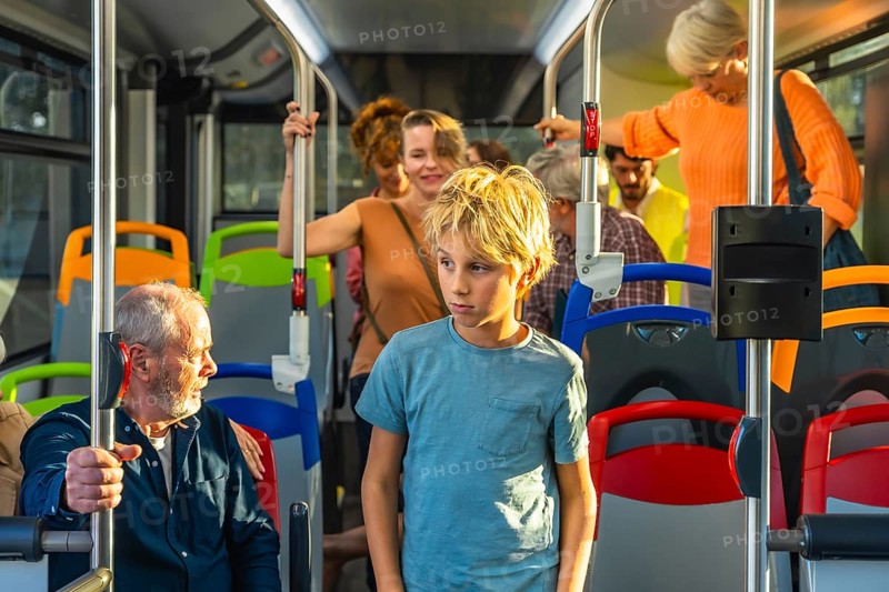 Young boy standing in a bus while other diverse passengers are commuting, experiencing urban public transport during daily life travel, showing people of different ages in motion