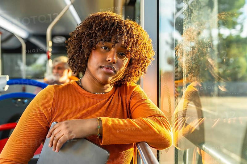 Young black woman with curly hair traveling on public transport, catching golden hour daylight during her daily commute, creating a thoughtful and relaxed atmosphere
