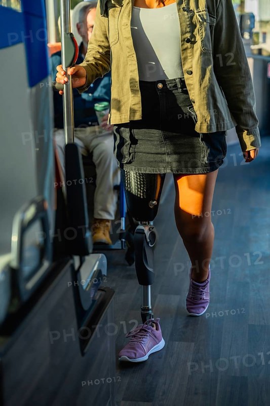 Woman with prosthetic leg and athletic shoe standing on a city bus, holding the handrail while commuting symbolizing mobility, independence, inclusion and urban accessibility