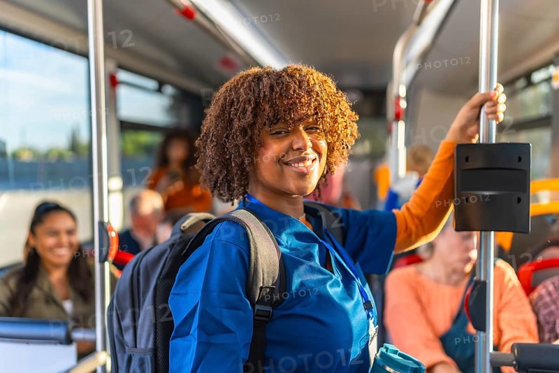 African american woman healthcare worker in blue scrubs carrying a backpack and smiling while riding public transportation, commuting to or from work by bus