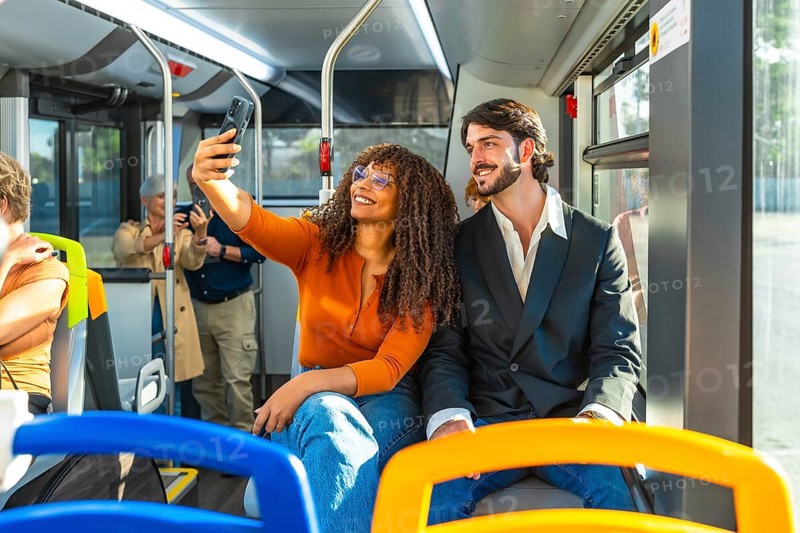 Diverse couple smiling and taking a selfie on a modern city bus during their commute, enjoying urban travel and capturing a candid moment with a smartphone