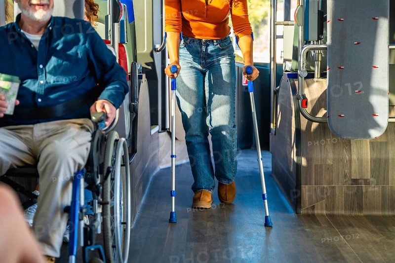 People with disabilities navigating public transportation, with one passenger using a wheelchair and another person walking with crutches inside a moving bus, emphasizing accessibility and inclusion
