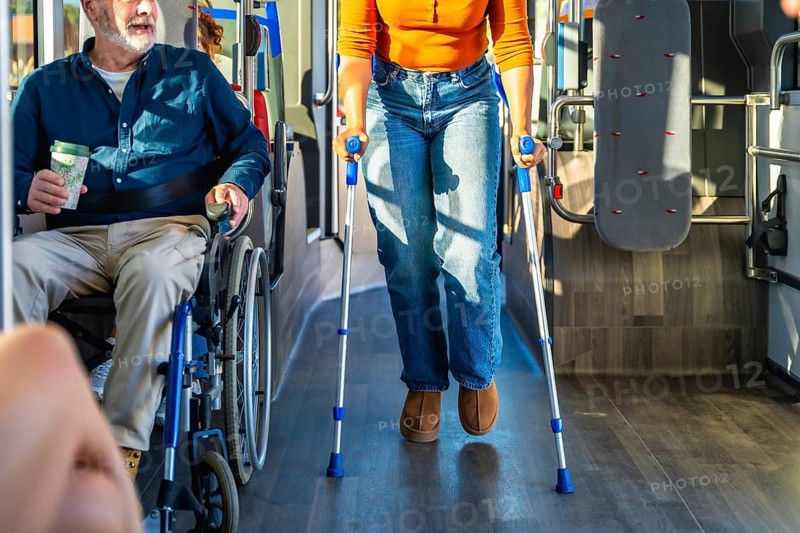 Senior man in wheelchair and woman with crutches navigate a busy city bus aisle together, illustrating accessible public transport, mobility, independence and inclusive commuting