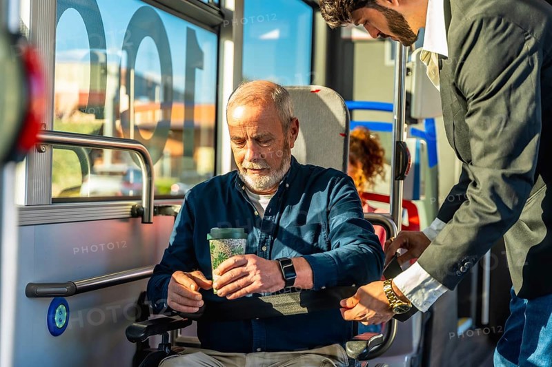 Young man assisting a senior passenger, ensuring safety and comfort while securing his wheelchair in a dedicated section of the accessible public transport bus, highlighting kindness and support