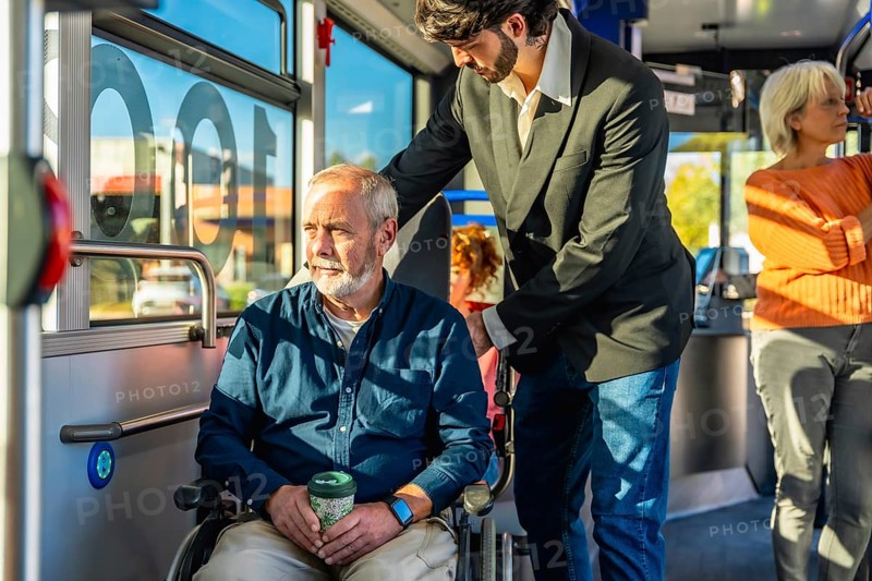 Young person assisting a senior man in a wheelchair on public transportation, ensuring accessibility and independent living while traveling through the city