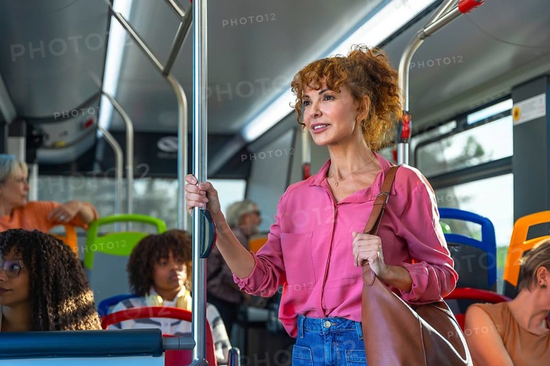 Mature woman standing and holding onto a pole inside a city bus, commuting to work or journeying through the urban environment, using sustainable transportation