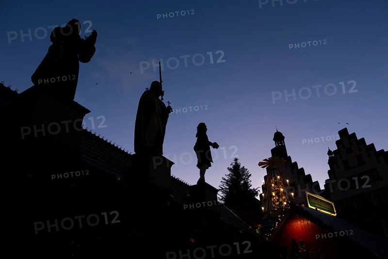 The silhouettes of the city greats Mrs. Rauscher (left), Charlemagne (center) and Johann Wolfgang Goethe (right), who are on the roof of a Christmas market stand on the Römerberg in Frankfurt am Main, stand out against the blue evening sky. The Frankfurt Christmas Market starts on November 24 and runs until December 22, Römerberg, Frankfurt am Main, Hesse, Germany