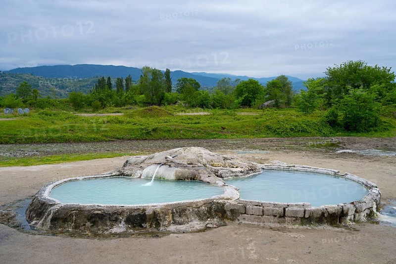 Hot spring pool in open landscape with wooded hills and mountains in the background, springs of Amaghleba, Dikhashkho Sulfur Geyser, hot sulfur springs of Wani, Vani, Imereti region, Georgia