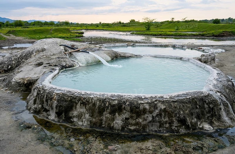 Hot spring pool in natural landscape with vast meadows and cloudy sky, springs of Amaghleba, Dikhashkho Sulfur Geyser, hot sulfur springs of Wani, Vani, Rioni River, Imereti region, Georgia