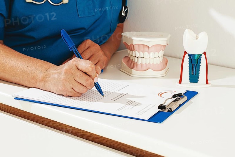 A dentist in a blue uniform studies patient information and prepares for treatment in a modern dental office