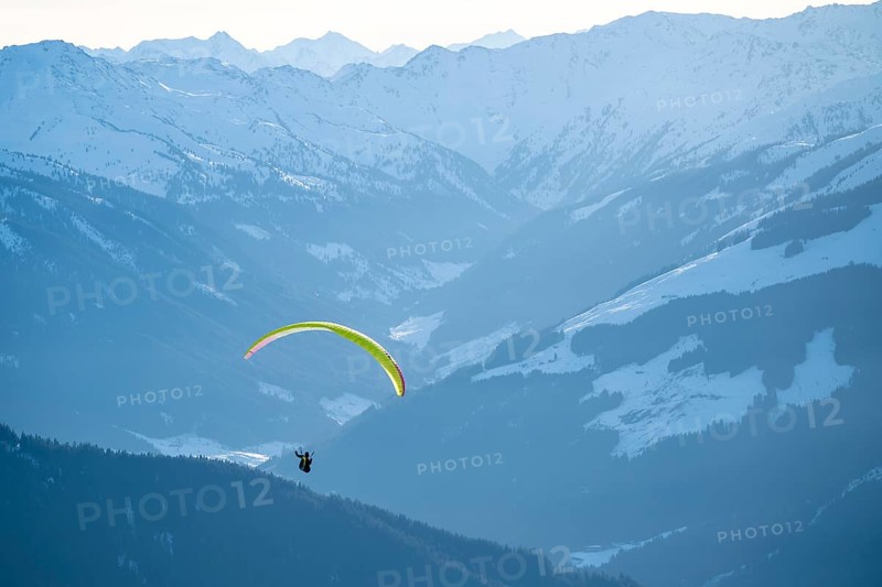Paragliders flying over snowy mountain peaks in winter in evening light, Kitzbühel Alps, Tyrol, Austria