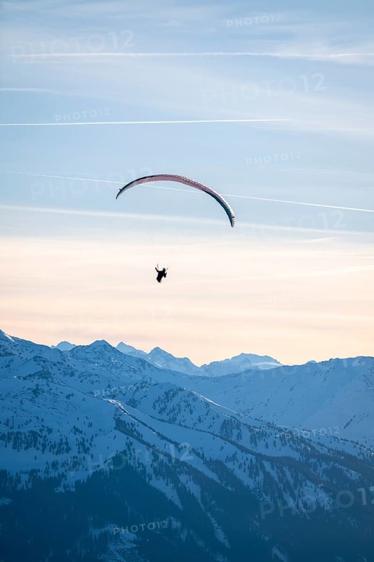 Paragliders flying over snowy mountain peaks in winter in evening light, Kitzbühel Alps, Tyrol, Austria