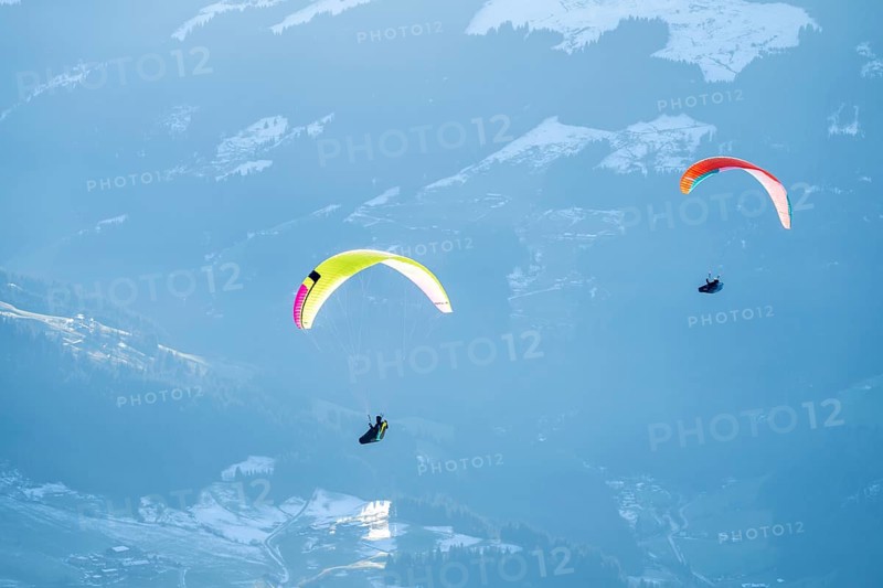 Two paragliders flying in front of snowy mountains in the evening light in winter, Kitzbühel Alps, Tyrol, Austria