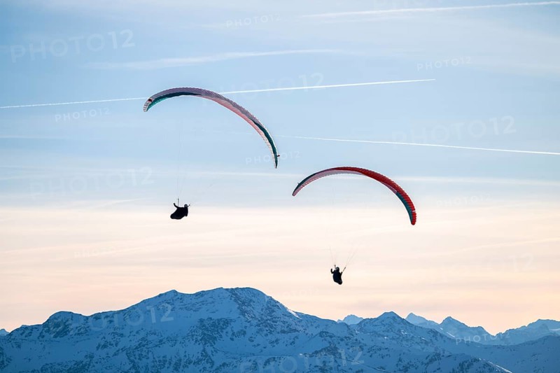 Two paragliders flying in front of snowy mountain peaks in the evening light in winter, Kitzbühel Alps, Tyrol, Austria