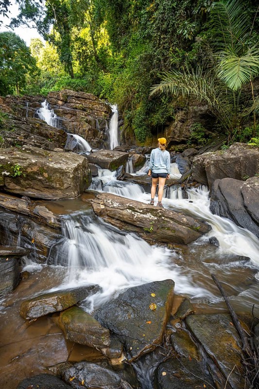 Tourist at Derema Waterfall, flows through dense vegetation, tropical rainforest in Amani Nature Forest Reserve, long exposure, Eastern Usambara Mountains, Tanga, Tanzania