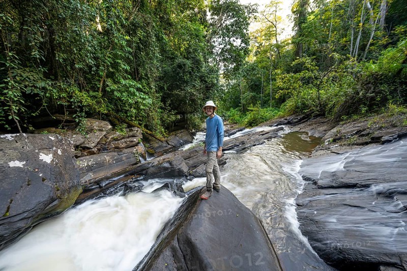 Tourist at Derema Waterfall flows through dense vegetation, tropical rainforest in Amani Nature Forest Reserve, long exposure, Eastern Usambara Mountains, Tanga, Tanzania