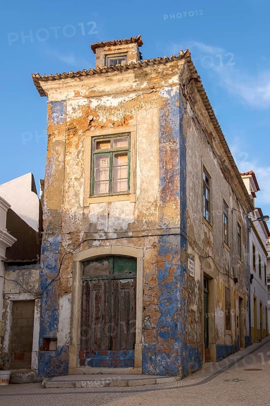 Abandoned building with peeling façade and blue paint residues under clear sky, Ericeira, Portugal