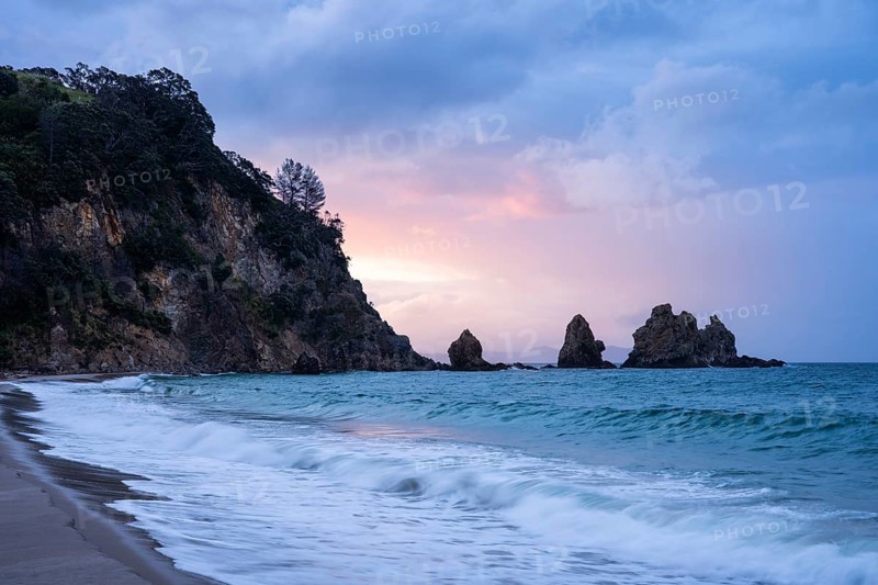 Landscape with sea, rocks and sandy beach in New Zealand in the evening at sunset. Otama Beach, Coromandel Peninsula, Waikato, New Zealand