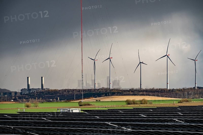86.5 MW peak open space photovoltaic systems, from RWE, with over 141, 000 solar modules, on a side strip, along the A44 motorway near Jüchen, at the timber triangle, recultivated open-cast mining area, in the background RWE brown coal power plant Neurath, wind farm, world highest wind measurement tower, 300m to research wind potential in the region, North Rhine-Westphalia, Germany