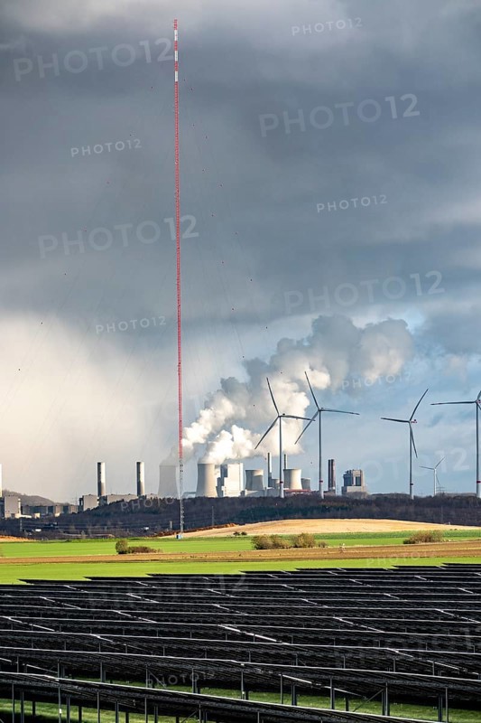 86.5 MW peak open space photovoltaic systems, from RWE, with over 141, 000 solar modules, on a side strip, along the A44 motorway near Jüchen, at the timber triangle, recultivated open-cast mining area, in the background RWE brown coal power plant Neurath, wind farm, world highest wind measurement tower, 300m to research wind potential in the region, North Rhine-Westphalia, Germany