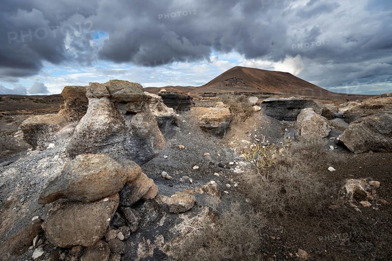Eroded rock formations in volcanic landscape with dramatic cloudy skies, Ciudad Estratificada or Los Roferos, Antigua Rofera de Teseguite, Lanzarote, Canary Islands, Spain