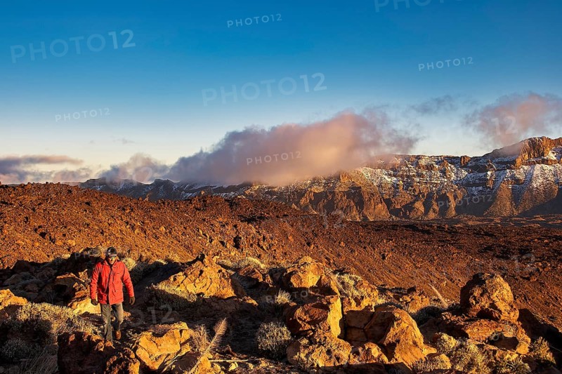 Person wearing a red jacket standing in front of a vast, sun-drenched mountain landscape, UNESCO World Heritage Site, Teide National Park, Tenerife, Canary Islands, Spain