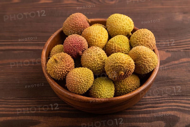 Ripe Lychee on clay bowl on brown wooden background, side view, close up, minimalism