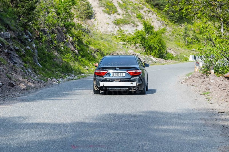 Black car driving on a winding road through the countryside, car without rear bumper, Georgia