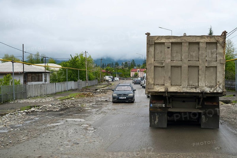 A truck and a car on a wet rural road with cloudy sky and mountains in the background, bad road in a village in Georgia