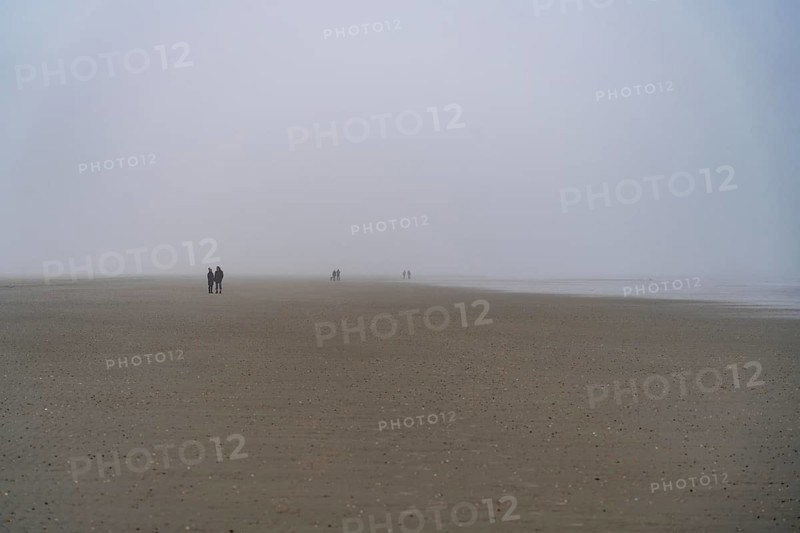 Walkers on the mudflats, in thick fog, near the East Frisian island of Spiekeroog, west of the North Sea island, at low tide, with a wind farm on the coast in the background, Lower Saxony, Germany