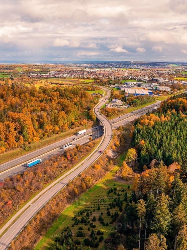 Aerial view of a road in autumn landscape with view of city and wooded area, A8 near Rutesheim, Germany