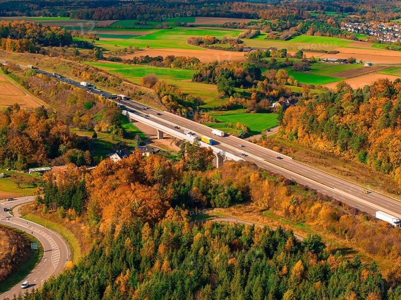 Road with bridge through autumn landscape with green fields and wooded hills, A8 near Rutesheim, Germany