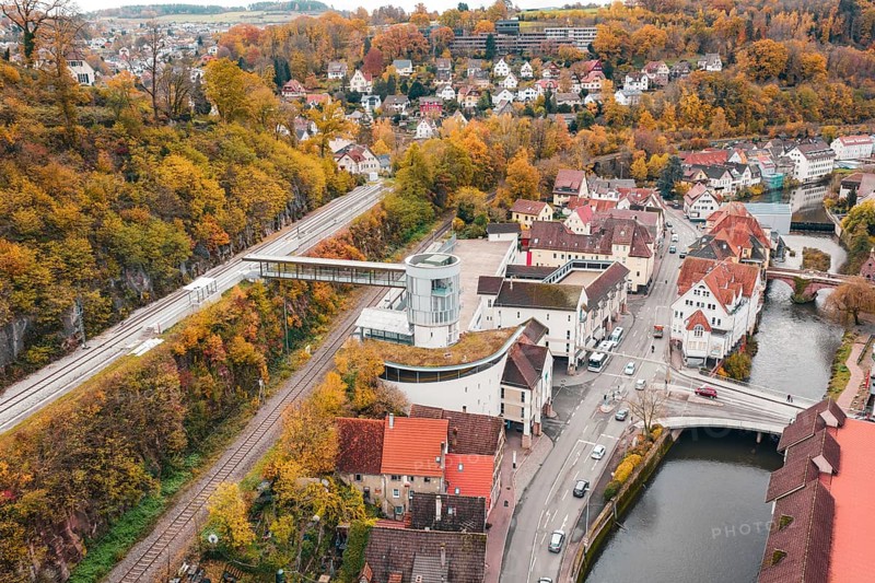 Idyllic small town in autumn colors with a river and bridge, surrounded by colorful trees. Railway station at the edge of the forest, Hermann Hessebahn, ZOB Calw, Germany