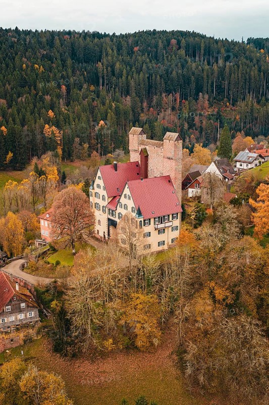 A castle with red tiled roofs surrounded by autumn-colored trees and small houses, Berneck Castle, Altentsteig, Calw district, Germany