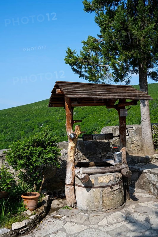 Rustic fountain with wooden roof surrounded by nature and plants in sunny weather, Motsameta monastery, near Kutaisi, Imereti region, Georgia
