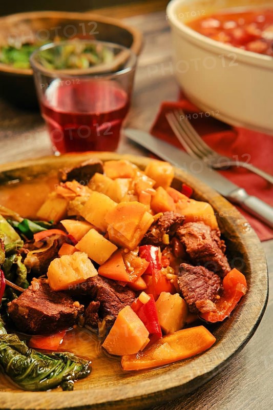 A hearty beef stew with tender chunks of beef meat alongside carrots and bell peppers is served in a rustic wooden bowl. The warm meal is perfect for a cozy dinner setting