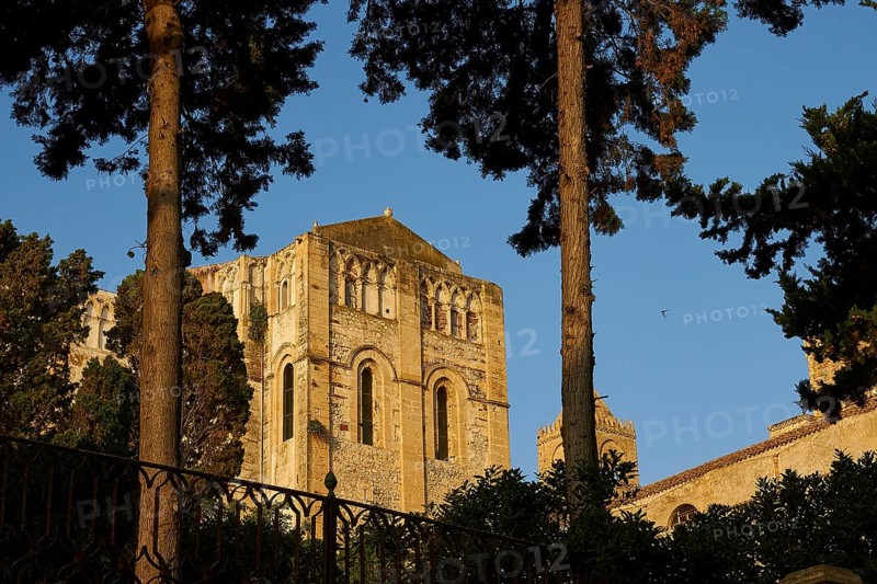 Historic Romanesque church surrounded by trees under clear blue sky at sunset, Cefalu, cathedral, UNESCO World Heritage Site, Sicily, Italy