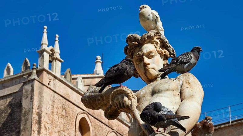 Marble sculpture with doves under a blue sky, in the background historic baroque style building, Monreale, cathedral, UNESCO World Heritage Site, Sicily, Italy