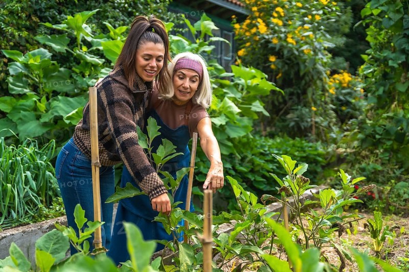 Mother and daughter bonding over gardening in their green home garden, learning about plants, sharing skills and smiles while nurturing vibrant foliage and enjoying sunny outdoor time
