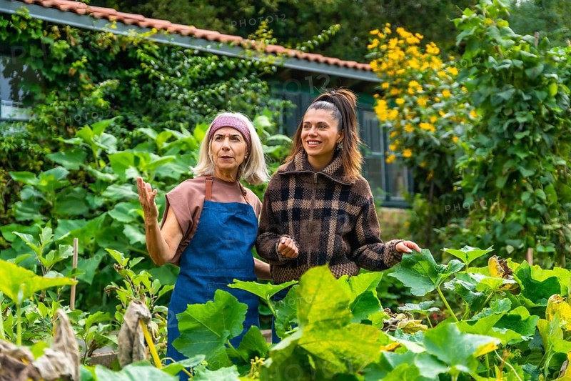 Mother and adult daughter enjoying time together in a lush green garden, the older woman teaching and sharing her gardening experience with the younger woman
