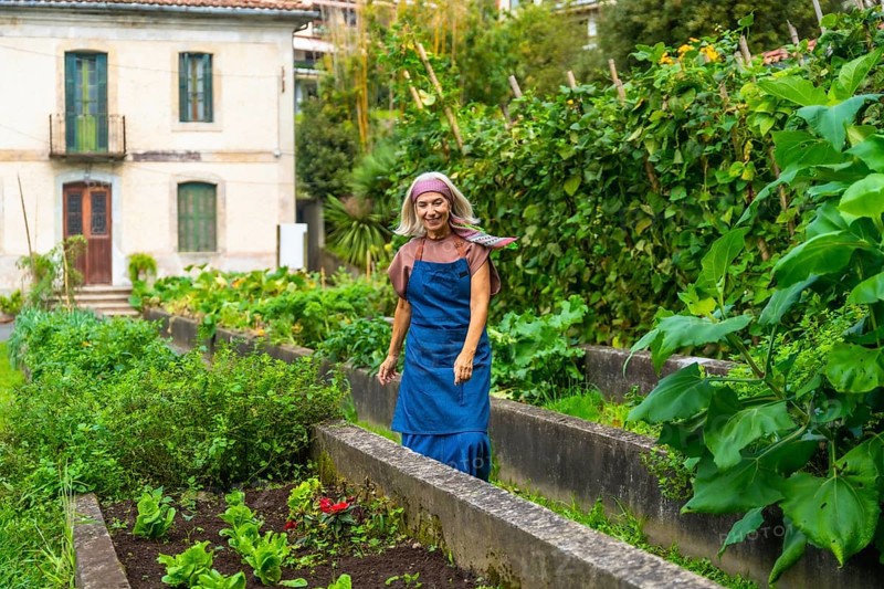 Senior woman smiling while walking through her bountiful urban vegetable garden, cultivating fresh organic produce in raised beds, embracing a sustainable lifestyle